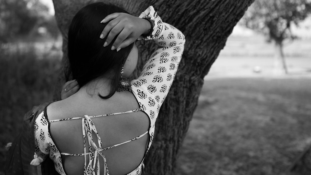 Woman leans against a tree, showing her back.