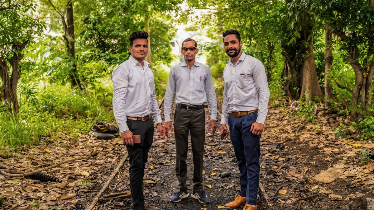 Three men in dress shirts pose confidently on a forest pathway, surrounded by lush greenery.